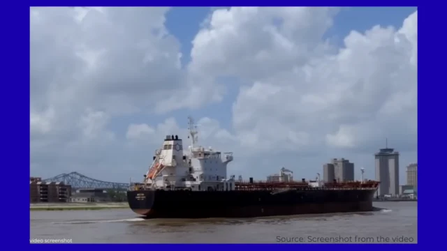 Oil tanker on a river near a city skyline.