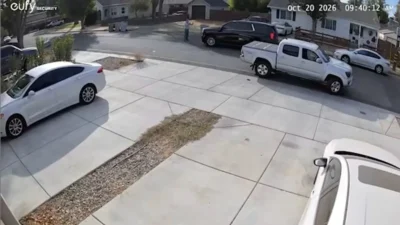 A pedestrian stands near a black SUV on a residential street in Woodland, California.